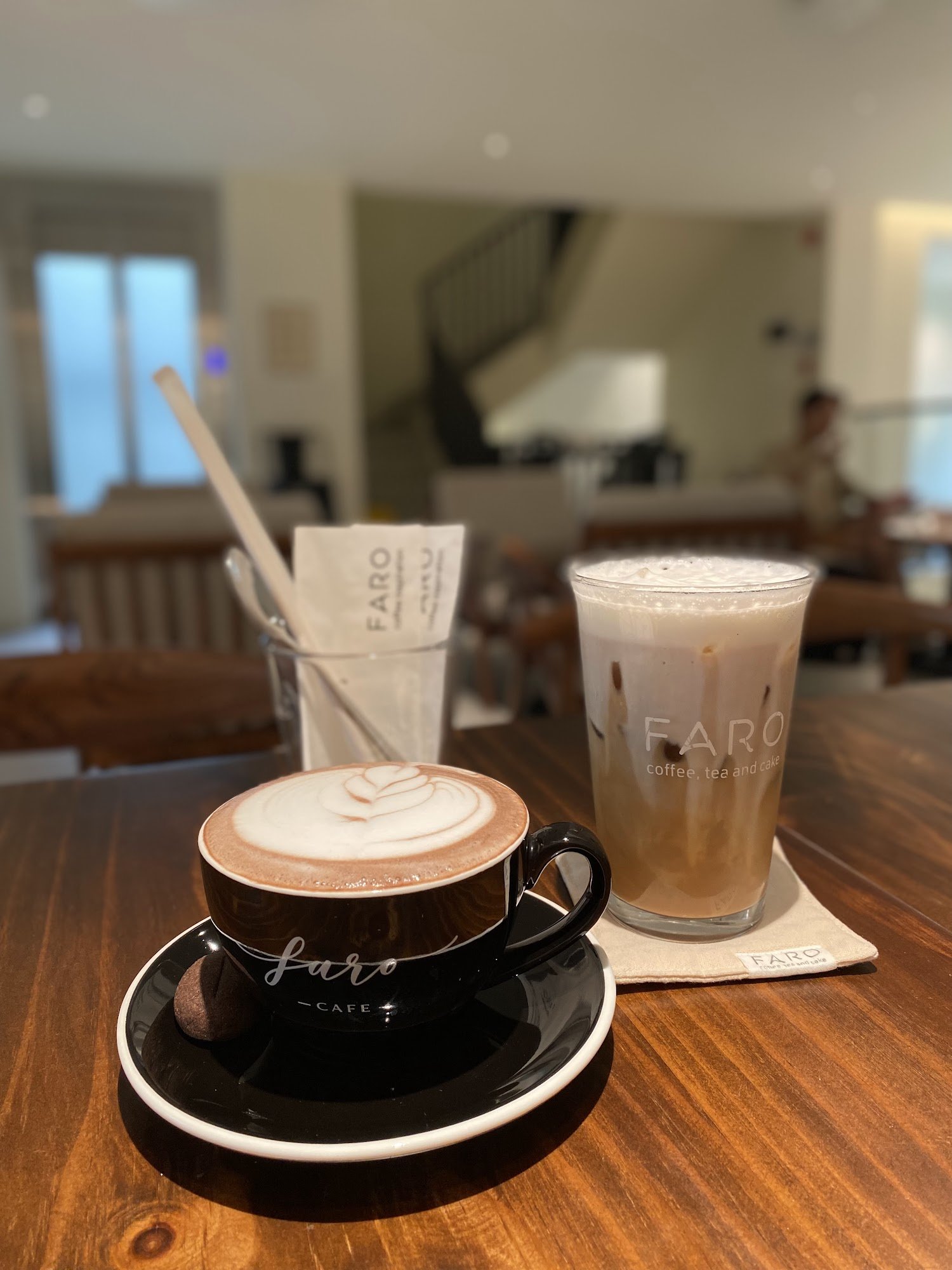The image shows a close-up of two beverages on a wooden table in what appears to be an indoor café setting.