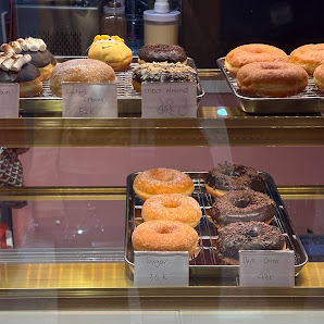 A display case in a bakery or café showcasing an assortment of donuts and pastries with visible price tags.