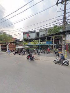 The image depicts a street scene in Thao Dien, Saigon. There are several motorcycles and scooters parked on the side of the road, with people sitting 