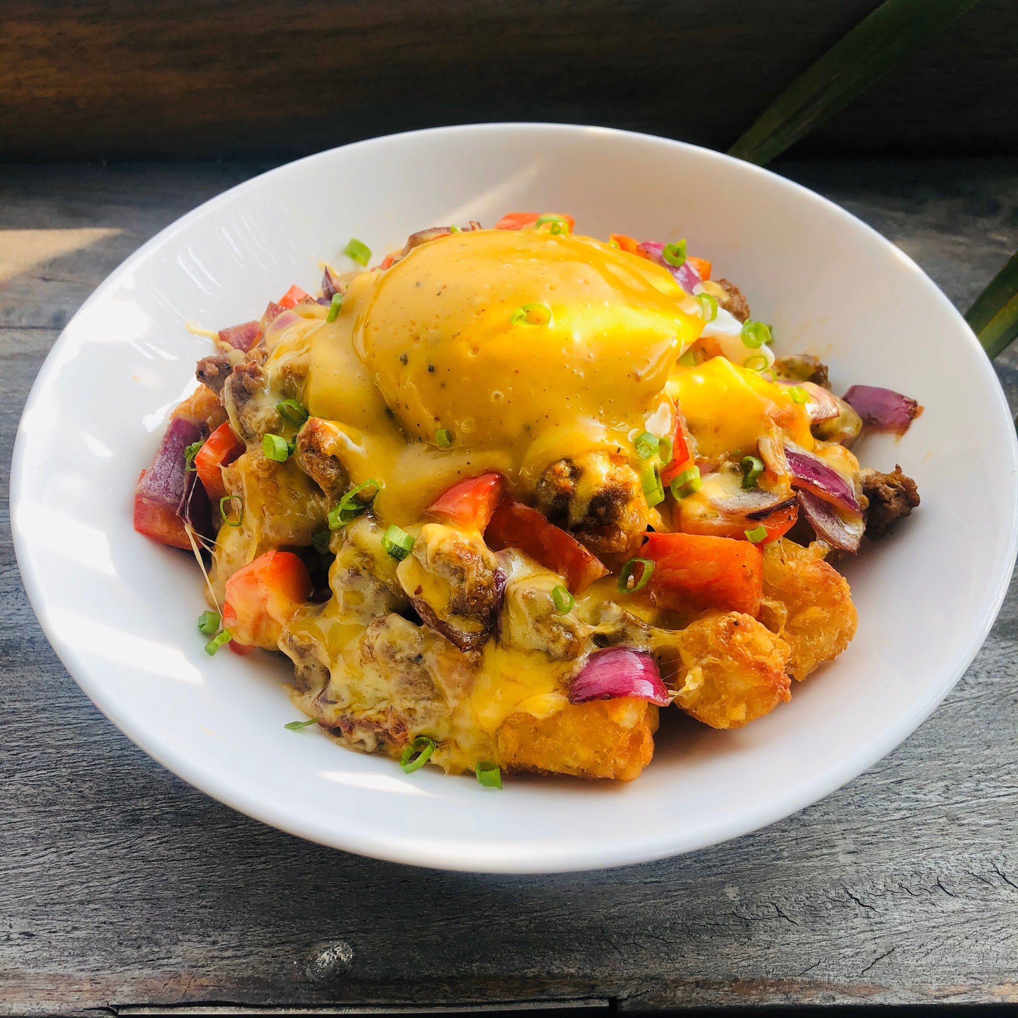A plated dish featuring a fried egg atop what appears to be hash browns or potato wedges mixed with diced vegetables such as red and green bell pepper