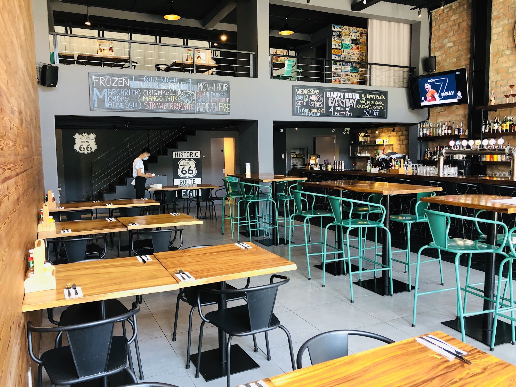 The image shows an interior view of a casual dining establishment featuring wooden tables and green chairs on the ground floor with additional seating
