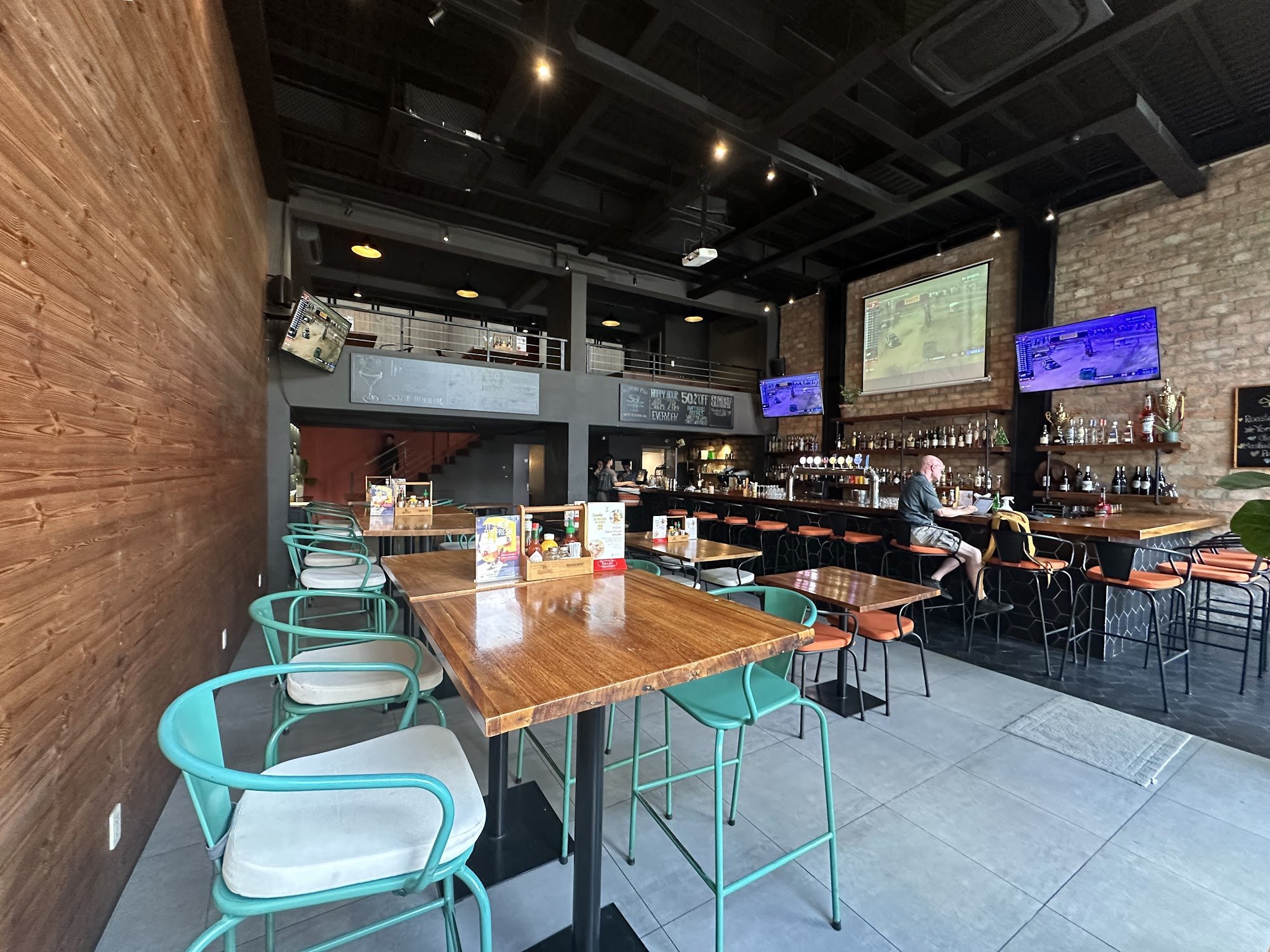 The image shows an interior view of a modern bar or pub setting in Thao Dien, Saigon. The space features exposed brick walls and wooden accents, with 