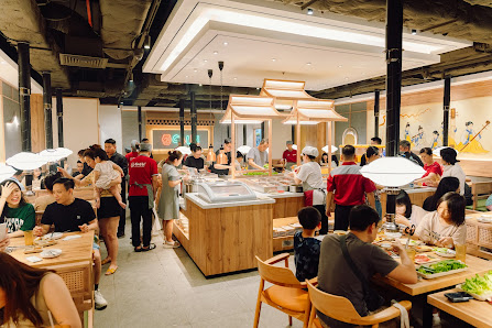 A bustling indoor dining venue in Thao Dien, Saigon, featuring a modern open kitchen setup with wooden counters, multiple food stations, and numerous 