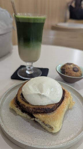 A dessert item consisting of a pastry topped with what appears to be cream and possibly chocolate sauce or syrup on the side, served alongside a green