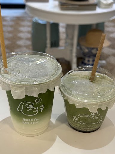 Two green-colored beverages in clear plastic cups with a white ruffled edge and straw lids, featuring cartoon dog illustrations on the front of each c
