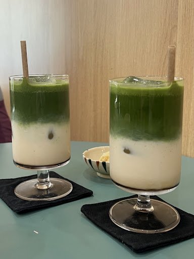 Two glasses of layered green tea latte on a table in what appears to be an indoor setting with wooden paneling.