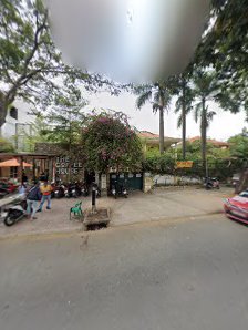The image shows an outdoor scene of a street in Thao Dien, Saigon with various elements such as trees, people sitting on benches and chairs, motorcycl