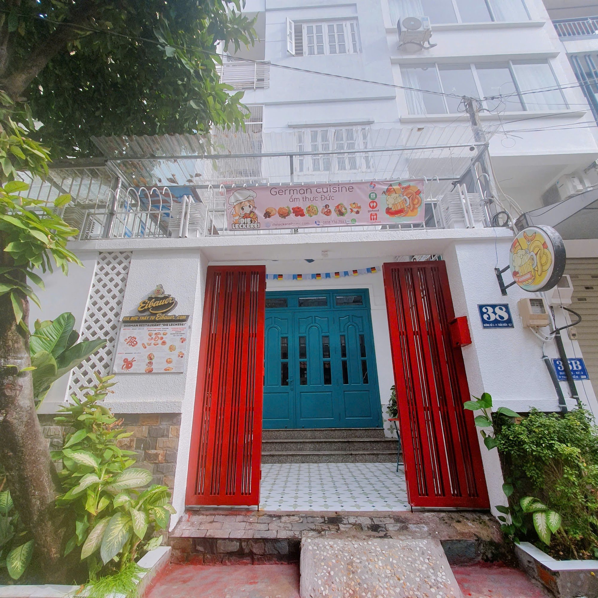 The image shows an exterior view of a building that appears to be a restaurant or cafe with the entrance marked by bright red doors and blue double do