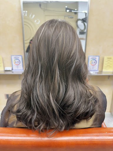 The image shows a person seated in what appears to be a hair salon or barber shop with their back facing the camera, displaying styled hair that is li