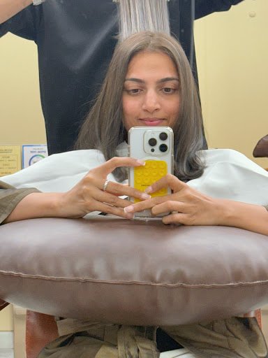 A person is sitting in a salon chair while taking a selfie using their smartphone.