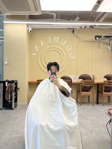A person is sitting in a barber's chair at an establishment named 'COURBEING'. The interior has beige walls with the name prominently displayed, and t