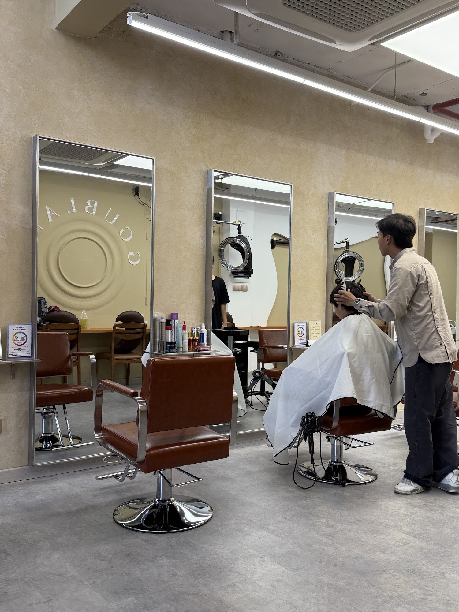 The image shows an interior view of a modern hair salon named 'CURLFIND'. It features two barber chairs, one with a customer receiving service and ano