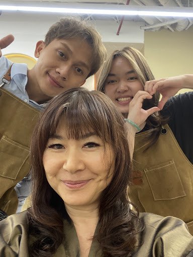 Three individuals are posing for a selfie in what appears to be an indoor setting. They all wear aprons and seem cheerful, suggesting they might work 