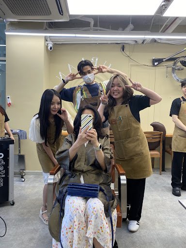 A group of four individuals in a casual setting, likely an office or workshop environment, with three standing and one seated on a chair. They are all