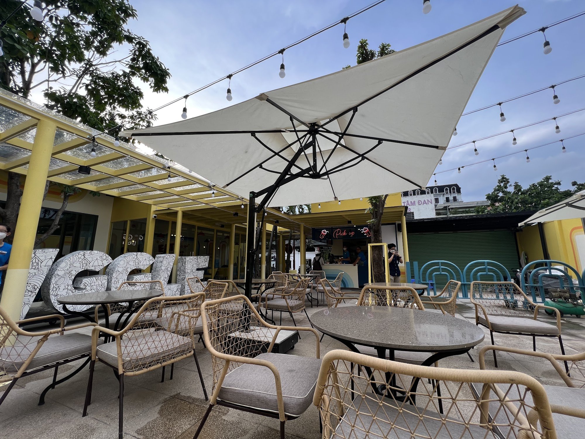 The image shows an outdoor seating area of a cafe or restaurant in Thao Dien, Saigon. The venue features several round tables with beige and white rat