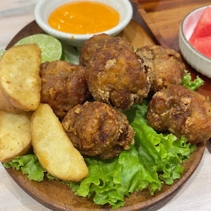 The image shows a plated dish consisting of several golden-brown meatballs served on green lettuce leaves with slices of potato and lime wedges beside