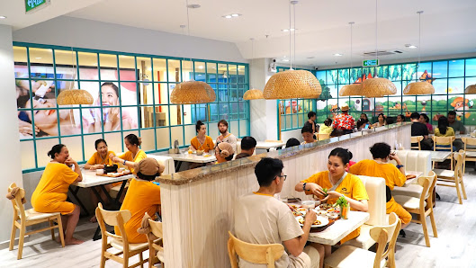 A bustling restaurant interior in Thao Dien, Saigon, featuring multiple tables with diners, staff in bright yellow uniforms serving food, modern decor
