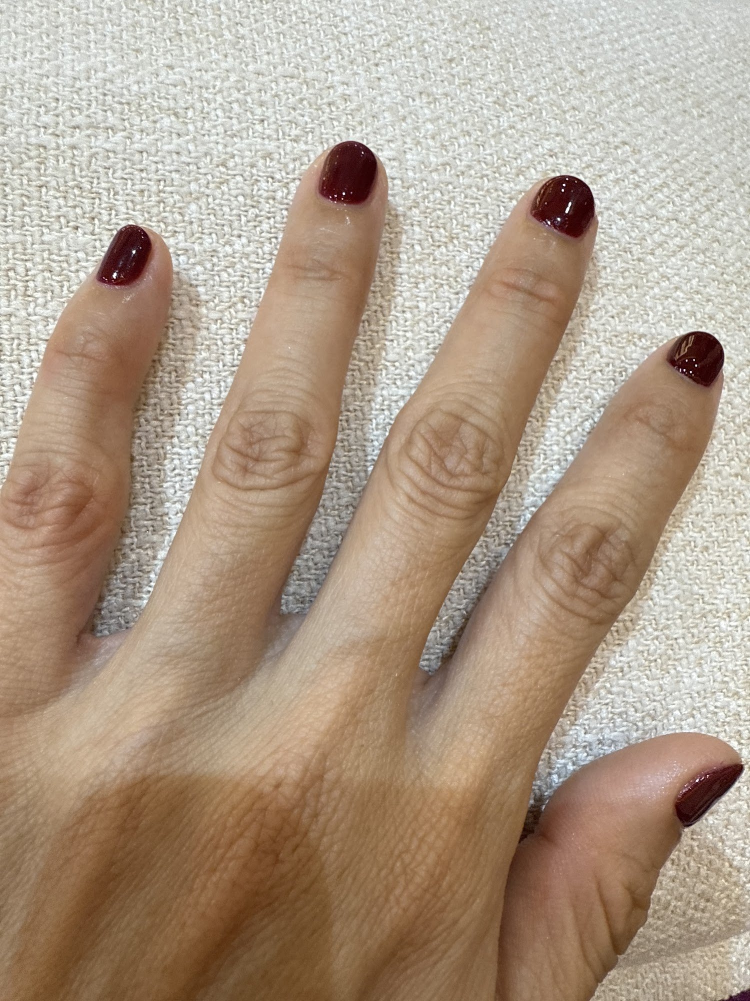 A close-up photograph of a person's hand displaying manicured nails painted in a glossy burgundy color.