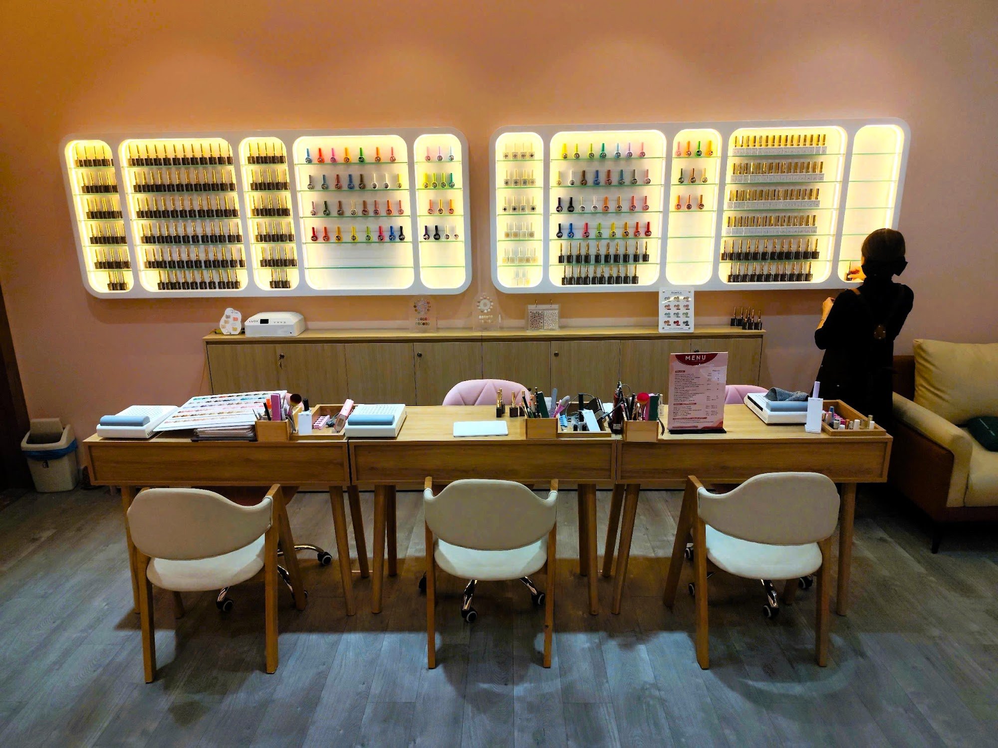 A well-lit nail salon interior in Thao Dien, Saigon. Features multiple illuminated shelves displaying various nail polish bottles in different colors 