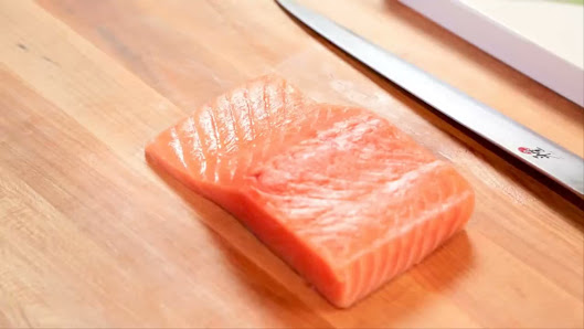 A piece of raw salmon on a wooden cutting board.