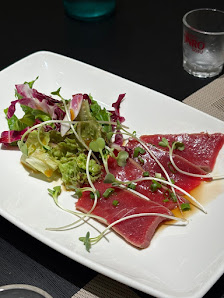 A plated dish consisting of thinly sliced raw meat and a side salad on a white rectangular plate.