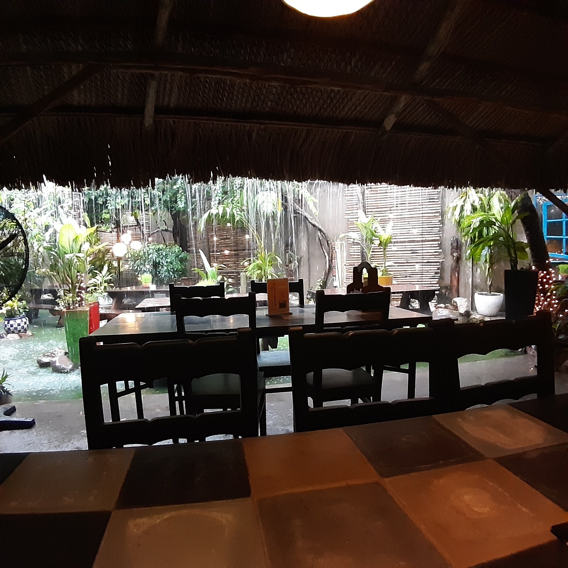 The image shows an interior view of a restaurant or cafe in Thao Dien, Saigon. The space is dimly lit with natural light filtering through the thatche