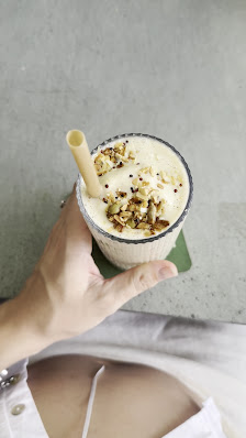 A hand is holding a bowl of creamy beverage topped with nuts and seeds.