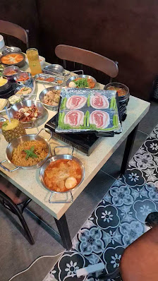 A dining table in a restaurant setting with various Vietnamese dishes including grilled meats, rice, soups, and side dishes. The table is surrounded b