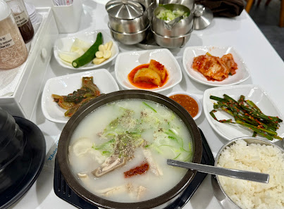 A table set for a meal featuring various Korean dishes including kimchi and banchan (side dishes), along with a bowl of rice, green vegetables, season