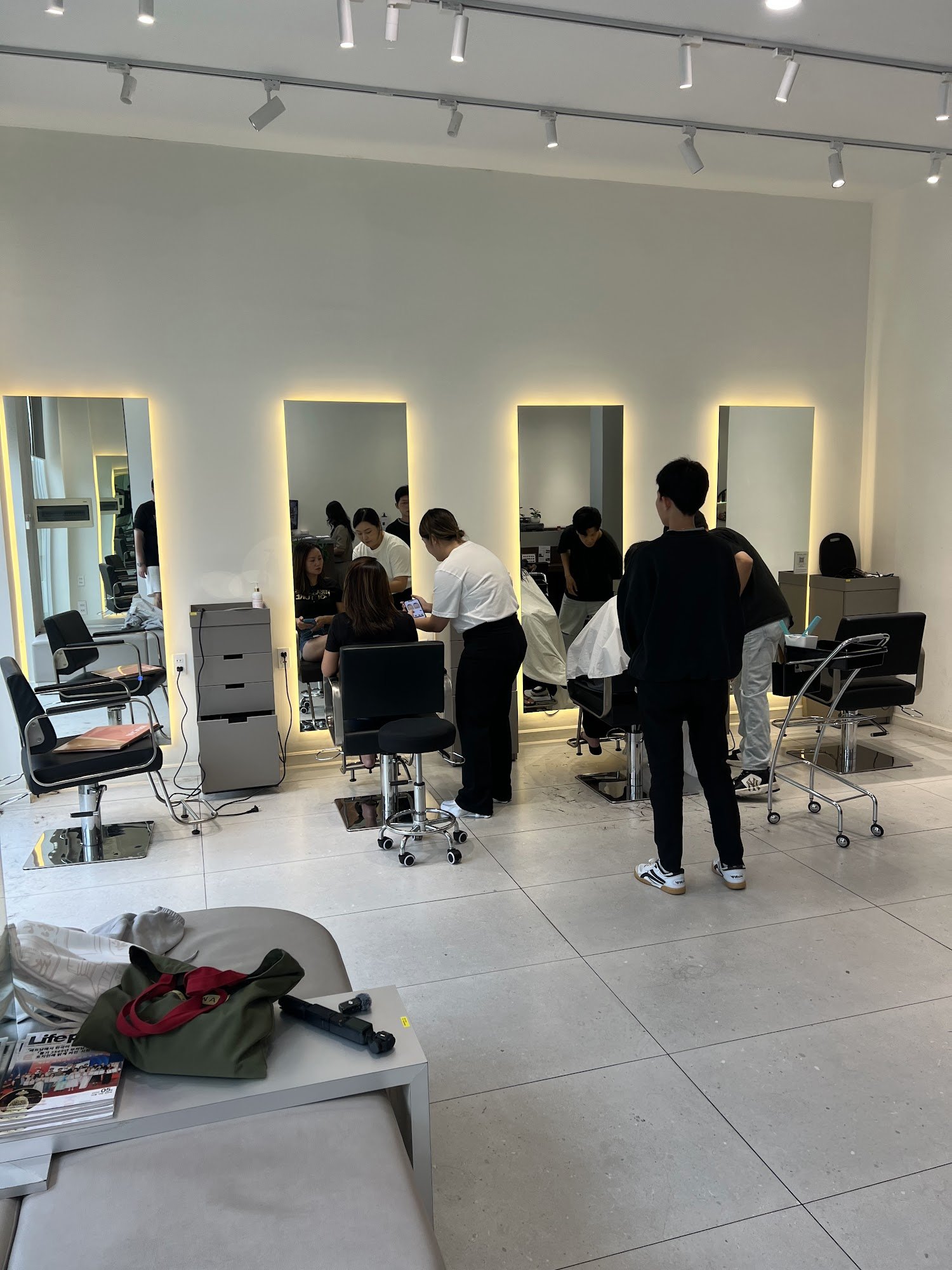 The image depicts an interior view of a modern hair salon located in Thao Dien, Saigon. The space is well-lit with track lighting and features multipl
