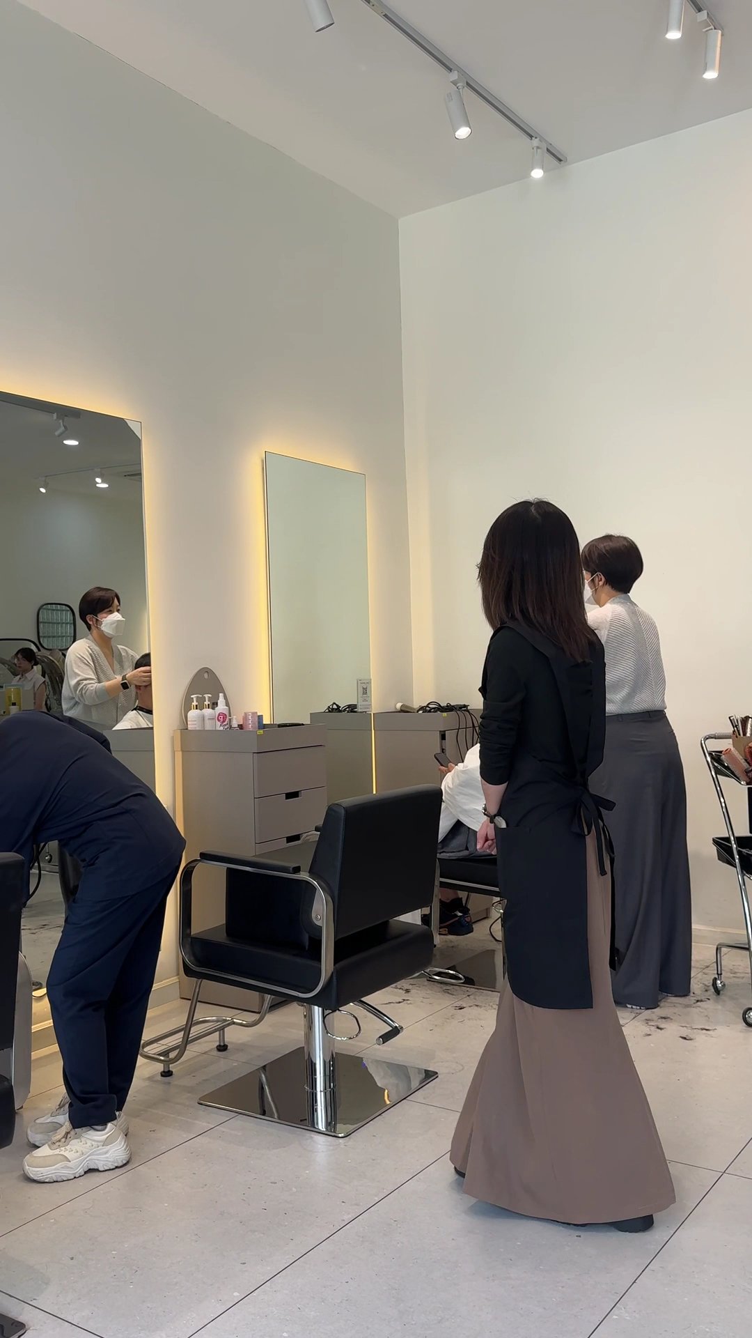 The image depicts an interior view of a modern hair salon or beauty parlor. The room is well-lit with white walls and features two large mirrors, one 