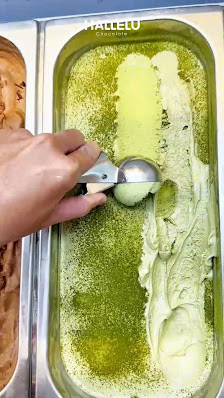 A close-up of a scoop being served from an ice cream dispenser labeled 'Hallelu'. The ice cream appears to be matcha flavored, with a vibrant green co