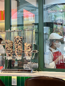 The image shows a food establishment's exterior view through large glass windows displaying various nuts in dispensers and staff members working insid