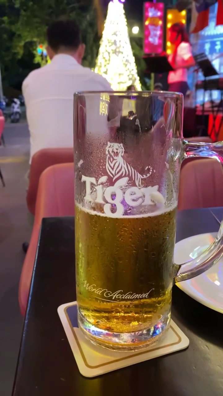 A close-up of a glass mug filled with beer on a coaster at an outdoor dining venue during nighttime.