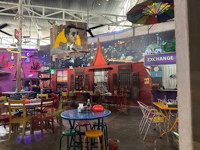 The image shows an interior view of a vibrant and eclectic restaurant or bar named 'Exchange'. The decor includes colorful murals, mismatched furnitur