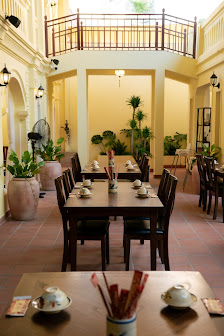 The image depicts an elegant interior dining space in a venue located in Thao Dien, Saigon. It features multiple dark wooden dining tables arranged in