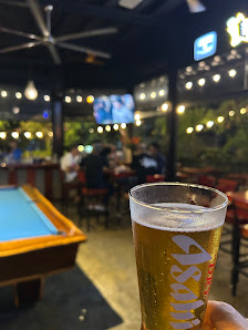 The image shows a casual bar setting in Thao Dien, Saigon, featuring patrons seated at tables and playing pool with a large screen displaying sports o