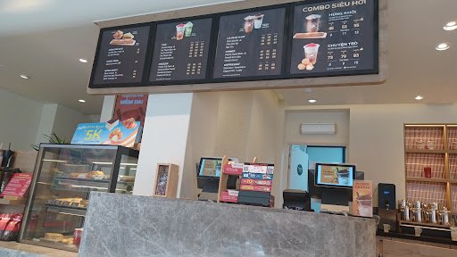 The image shows an interior view of a modern fast-food restaurant or cafe counter area with digital menus displaying various food and drink options.