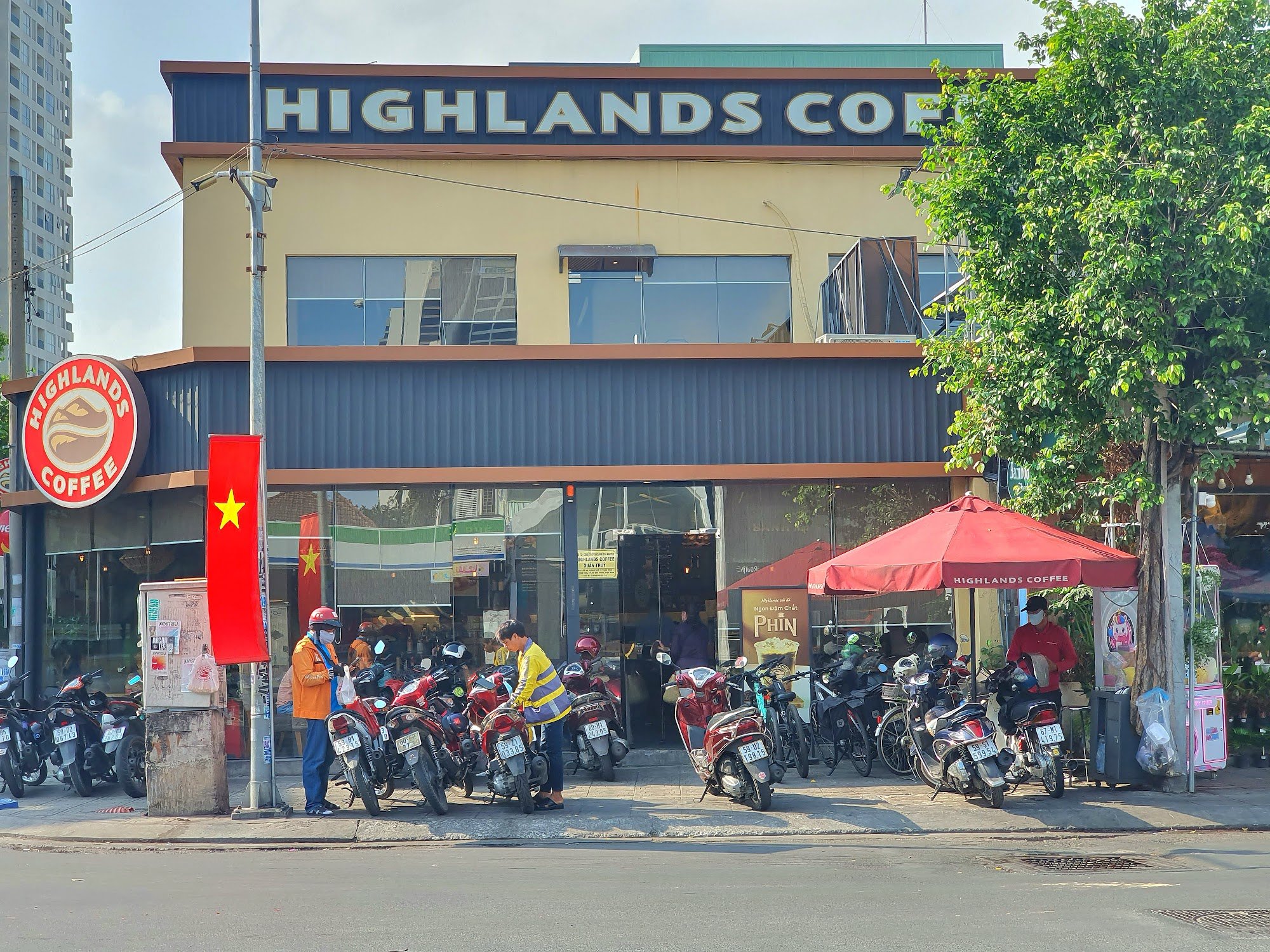 The image depicts the exterior of a Highlands Coffee shop located in Thao Dien, Saigon. The building has a two-story structure with a prominent "HIGHL