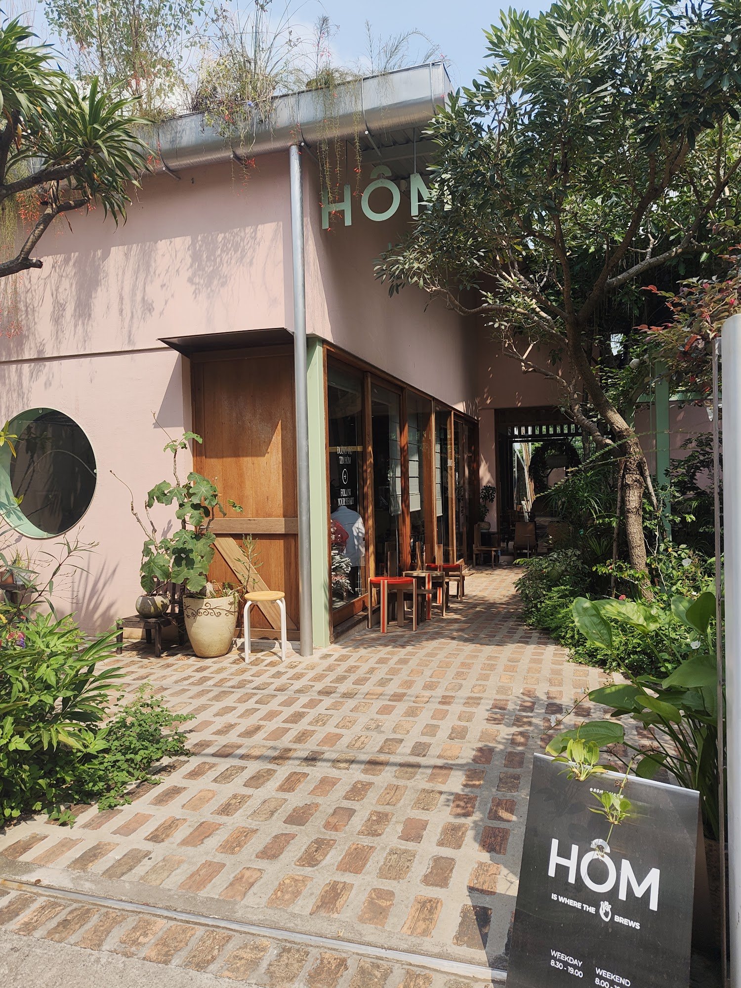 The image shows an exterior view of a cafe named 'HÔM' located in Thao Dien, Saigon. The establishment has a modern and cozy design with wooden elemen