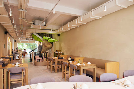 The image depicts the interior of a modern restaurant in Thao Dien, Saigon. It features wooden tables and chairs with light purple cushions, arranged