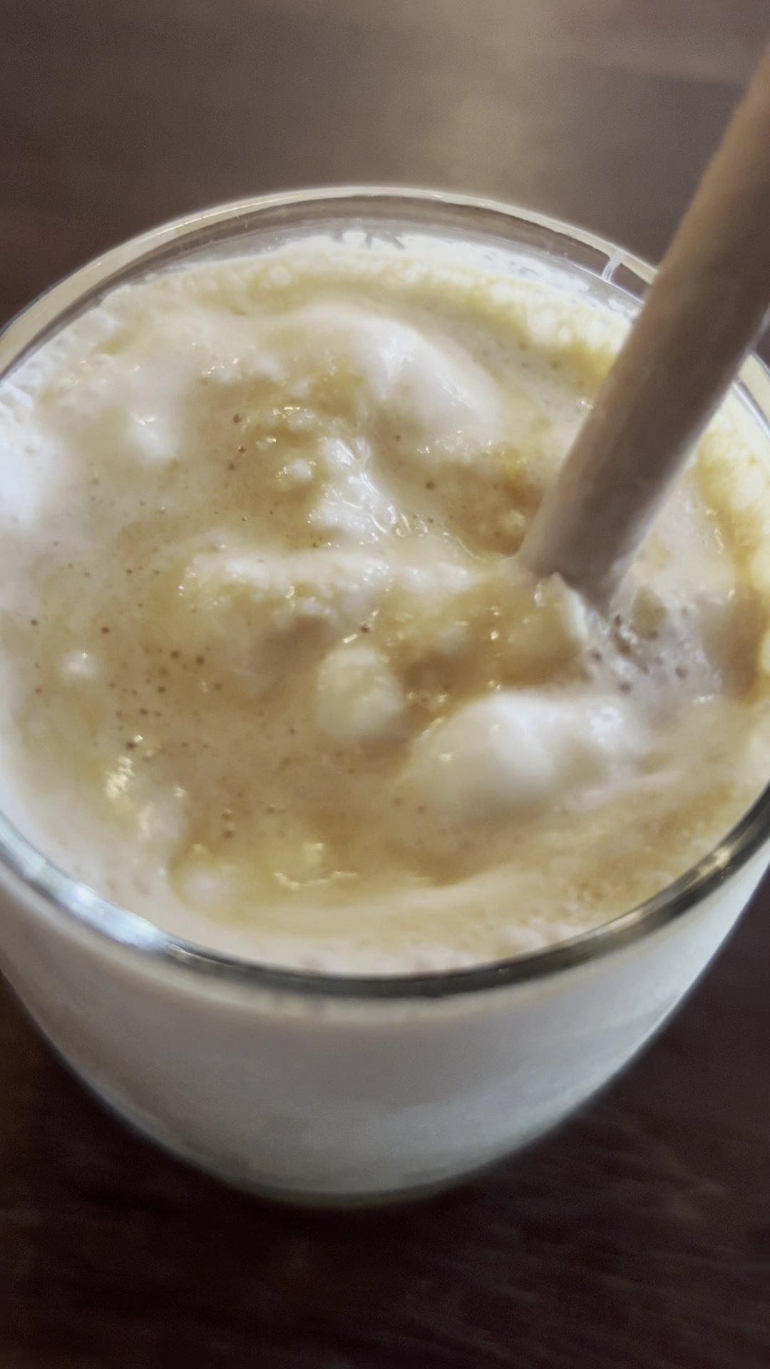 A close-up of a frothy beverage in a glass cup with a straw.
