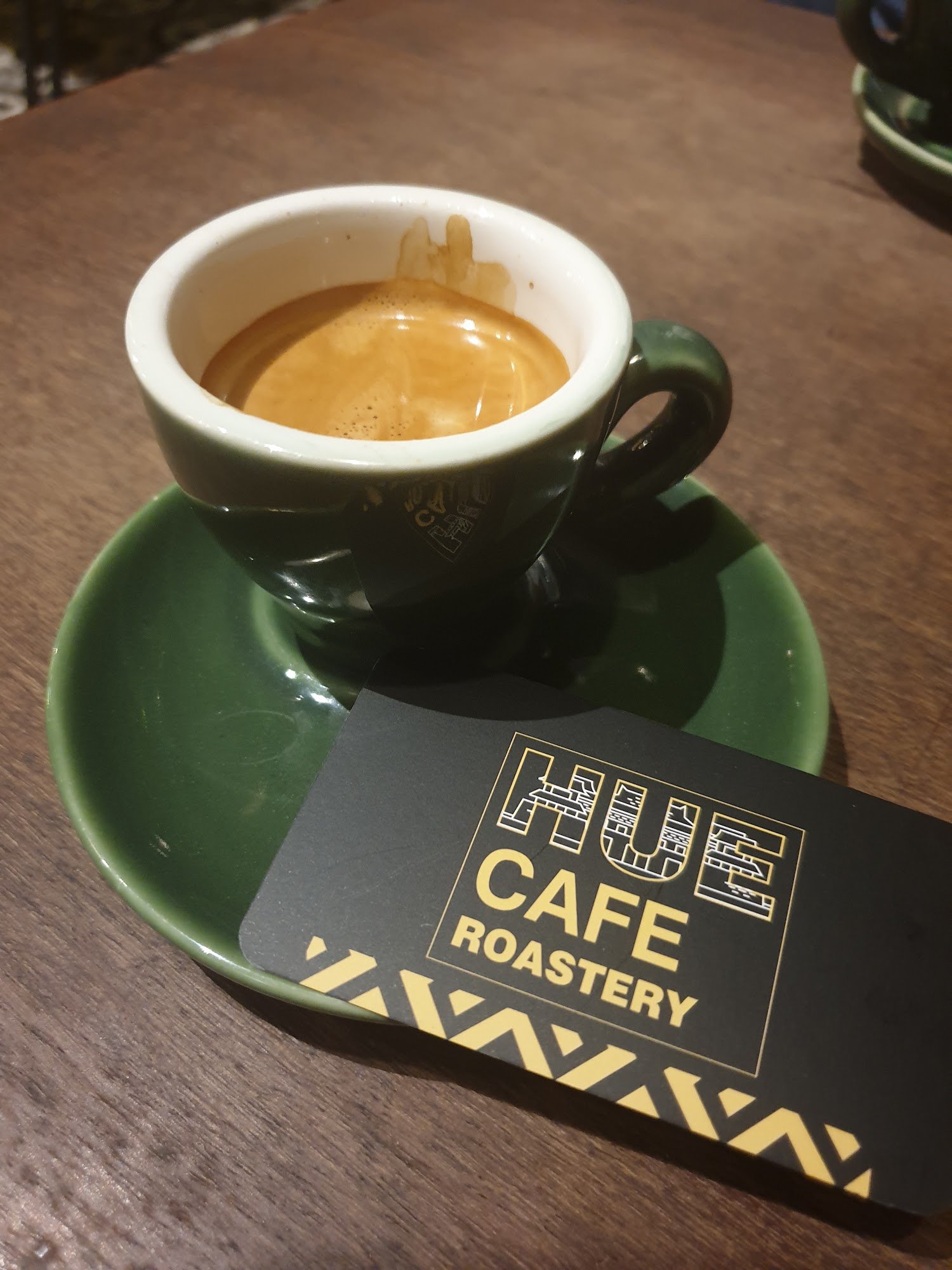 A cup of coffee on a green saucer from Hue Cafe Roastery is placed prominently in the foreground.