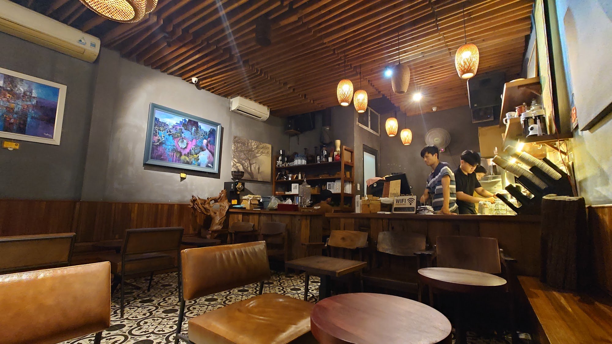 The image depicts an interior view of a cozy café or coffee shop. The space features wooden beams on the ceiling and walls, creating a warm atmosphere