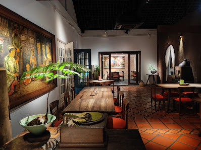 An interior view of a venue in Thao Dien, Saigon, featuring a long wooden dining table with red chairs, a large colorful mural on the left wall, potte