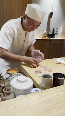 A person in a chef's uniform is preparing food on a wooden counter.