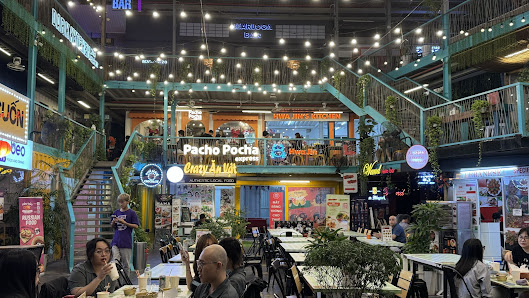 The image shows an indoor dining area of a restaurant named 'Pacho Pocha'. The venue has multiple levels with green railings and is well-lit, featurin