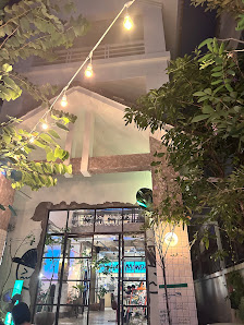 The image depicts the exterior of a venue in Thao Dien, Saigon. It features a building with a glass entrance door, string lights hanging above, lush g