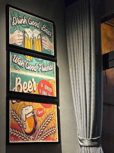 Three framed vintage-style posters on a wall. Top poster: 'Drink Good Beer' with hands holding beer mugs. Middle poster: 'With Good Friends Beer' with