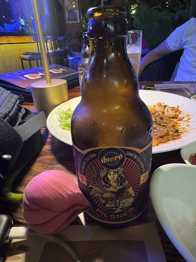A bottle of beer labeled 'Ibiero' sits on a table in what appears to be an indoor dining setting with dim lighting and other diners present.